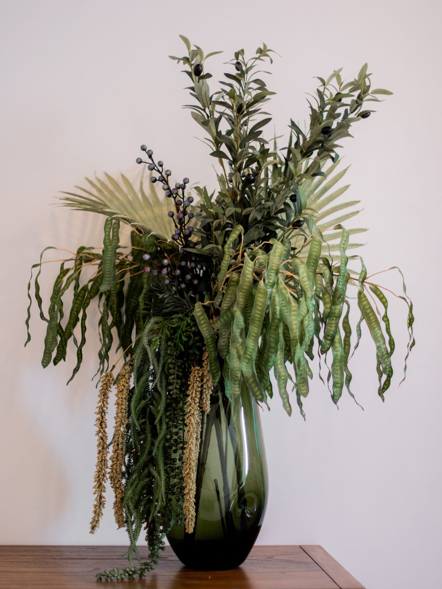 Composición botánica permanente con follaje colgante en florero de vidrio verde
